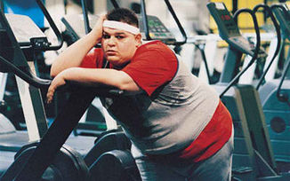 hombre con sobrepeso-obesidad, con gesto de aburrimiento, descansa sobre máquina de hacer ejercicio